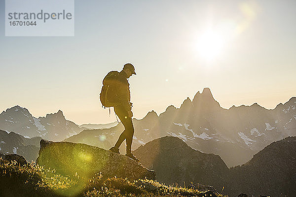 Rucksacktourist auf einem Berggipfel bei Sonnenuntergang.