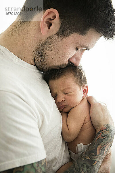 Close Up Side View of Tattooed Millennial Dad Kissing Newborn Sohn