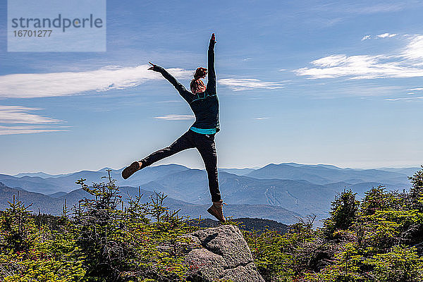 Junge Frau springt auf dem Gipfel eines Berges.
