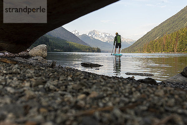 Ebenerdiger Blick auf einen Mann auf einem SUP-Board auf einem ruhigen Bergsee