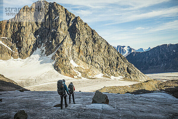 Zwei Rucksacktouristen überqueren einen Gletscher unterhalb einer Bergkette.