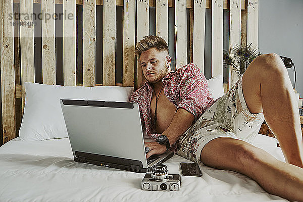 ein Mann arbeitet mit seinem Laptop in einem Hotelbett.