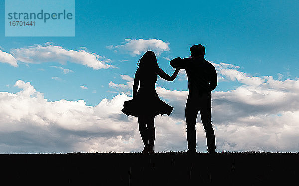 Silhouette eines Mannes und einer Frau  die gegen einen blauen Himmel mit Wolken tanzen.