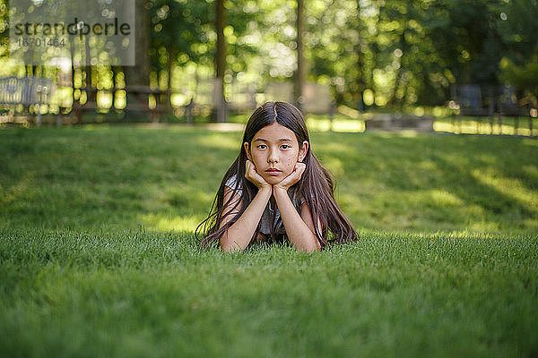 Ein Mädchen zwischen zwei Jahren liegt im Gras und stützt ihren Kopf in die Hände