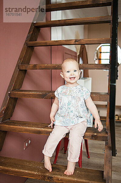 Cute lächelnde Baby-Mädchen sitzt auf Holztreppe in modernen appartment.