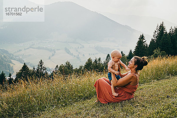 Mutter lächelt mit ihrem kleinen Kind im Gras sitzend