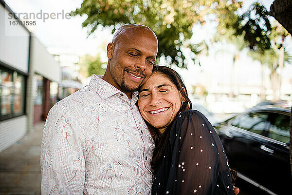Multirassisches Paar in den späten Vierzigern umarmt sich auf dem Bürgersteig von San Diego