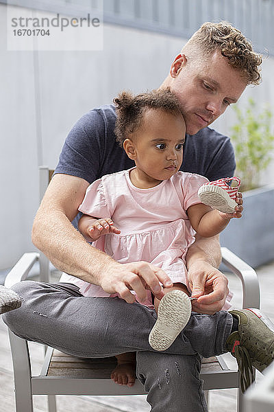 Ein Vater hilft seiner kleinen Tochter beim Anziehen ihrer Schuhe