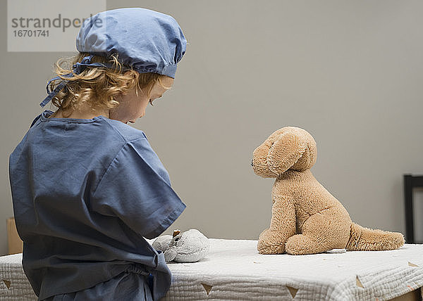 Kleines Kind in medizinischer PSA kümmert sich um einen Patienten mit Plüschhund
