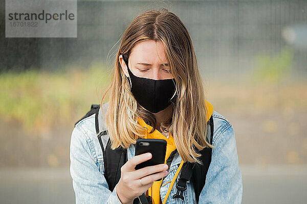 Frau mit Maske und Mobiltelefon. Junge Frau mit Smartphone und