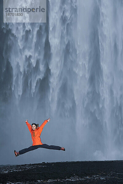 Frau springt vor dem Skógafoss-Wasserfall in Südisland