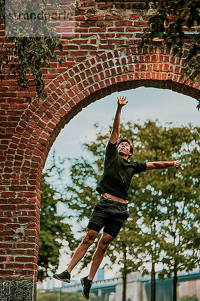 Junger Mann springt im Freien im Park hoch.