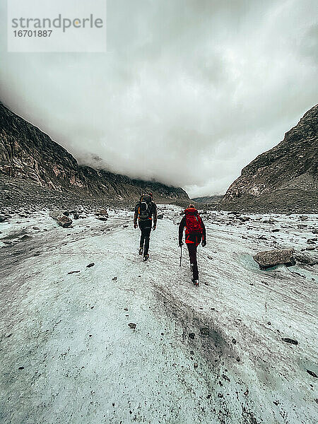 Zwei Bergsteiger wandern auf einem Gletscher unter bewölktem Himmel