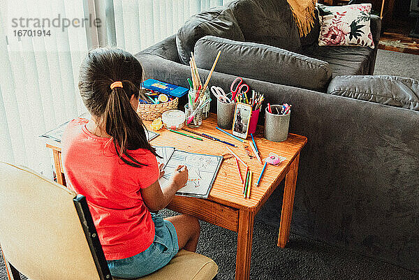 Multi racial 8 Jahre altes Mädchen sitzt am Schreibtisch Färbung & Gesicht Timing