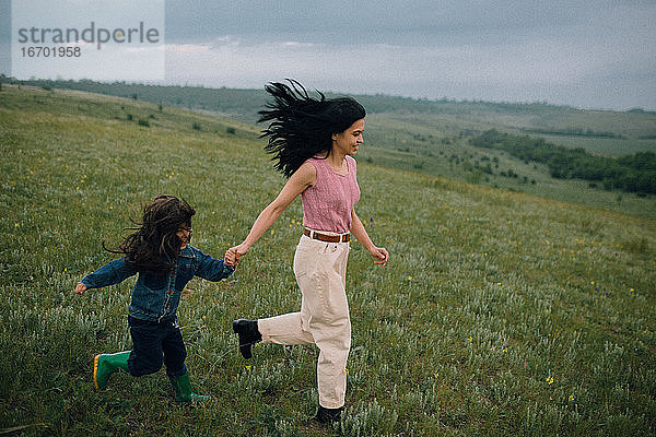 Mutter und Tochter laufen in der Natur einen Hügel hinunter