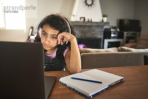 Ein gelangweiltes Mädchen macht seine Hausaufgaben mit seinem Laptop