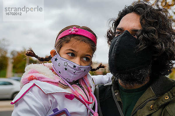 Vater und Tochter mit Schutzmasken und Halloweenkostüm