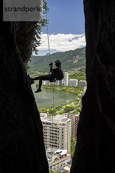 Blick auf die Silhouette einer Bergsteigerin  die sich an einem Riss im Berg abseilt