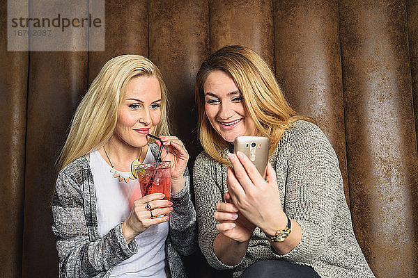 Freundinnen surfen auf dem Sofa in einer Bar auf ihrem Smartphone