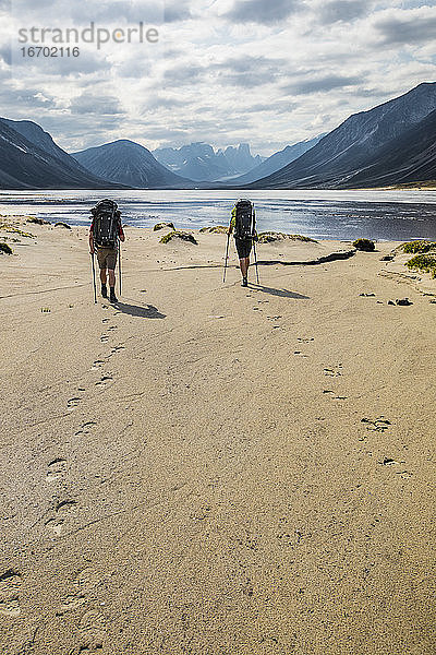 Rucksacktouristen hinterlassen Fußabdrücke im Sand am Akshayak Pass