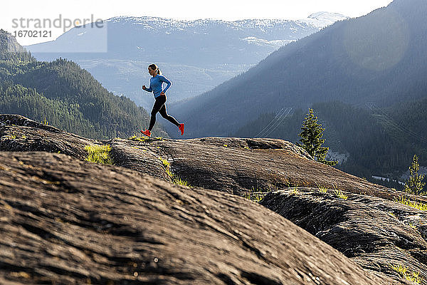 Seitenansicht einer starken Sportlerin  die während eines Fitnesstrainings auf dem Lande bei Sonnenuntergang gegen einen verschneiten Bergrücken läuft.