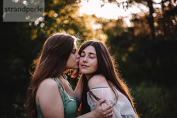 Junge Frau küsst ihre Freundin auf die Wange im Wald im Sommer