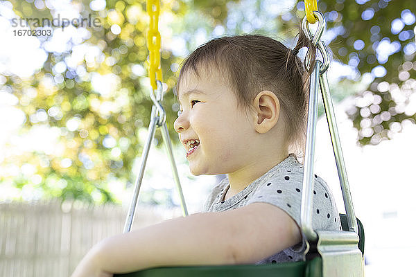 Side View of Little Girl Sitting in Backyard Swing Lächeln