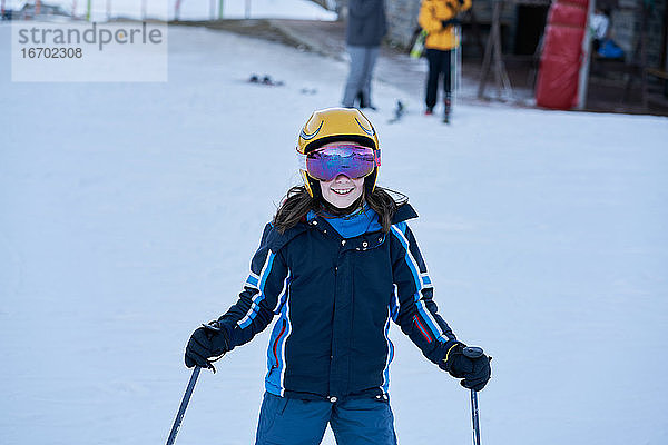 Mädchen mit Helm und Brille schaut lächelnd auf einer Skipiste