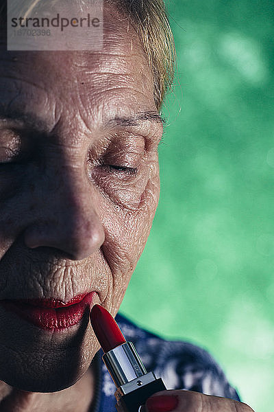 Alte Frau im Vordergrund mit rotem Lippenstift auf grünem Hintergrund