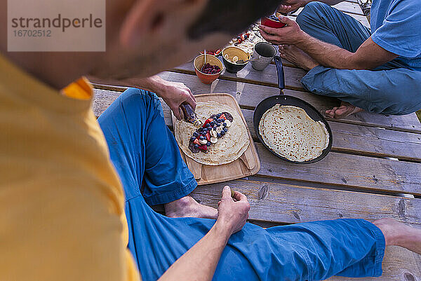 Mann gießt Ahornsirup auf süßen Crêpe  der auf einem Holzgestell sitzt