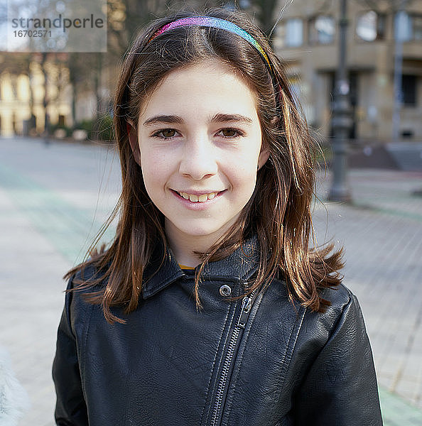 Porträt eines Mädchens auf der Straße  das mit einer schwarzen Jacke in eine Kamera schaut