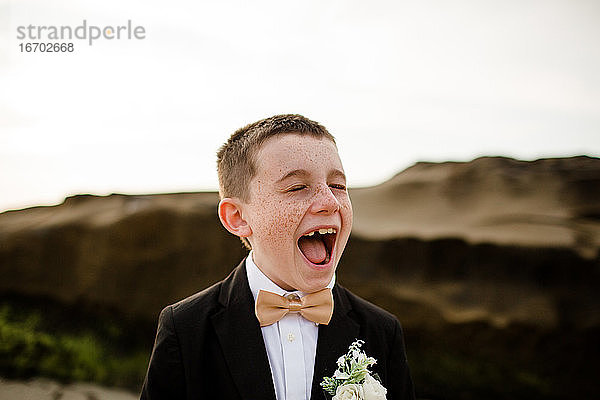 Neun Jahre alter Junge im Smoking lachend und stehend am Strand in San Diego