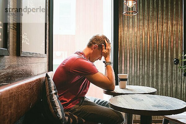 ein Mann saß gestresst und mit dem Gesicht in den Händen in einem Café