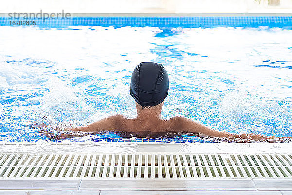 Junger Teenager mit weißer Mütze  der sich in einem Schwimmbad im Spa entspannt