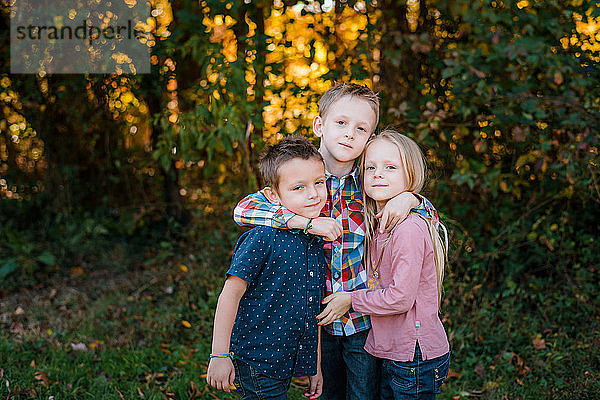 Bruder umarmt Geschwister draußen in der Natur Familienporträt