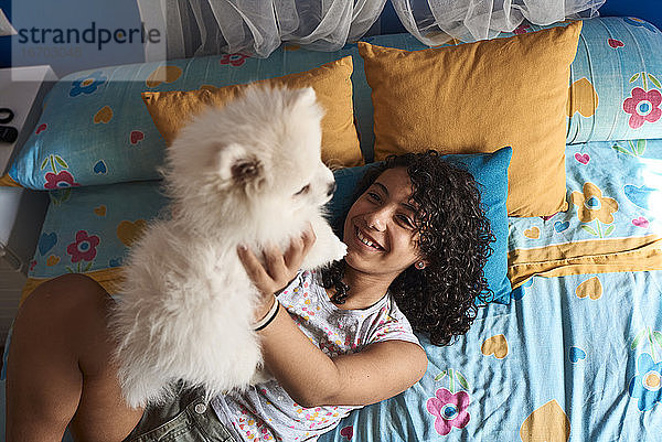 Ein kleines Mädchen spielt mit ihrem weißen Pomeranian-Welpen im Bett.