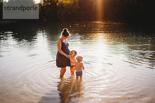 Schwangere Frau mit Kindern im Wasser am See mit goldenem Licht