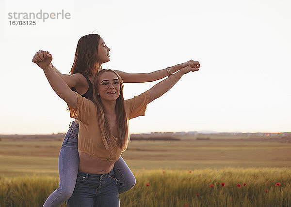 zwei Frauen halten sich bei Sonnenuntergang auf einem Feld an den Händen