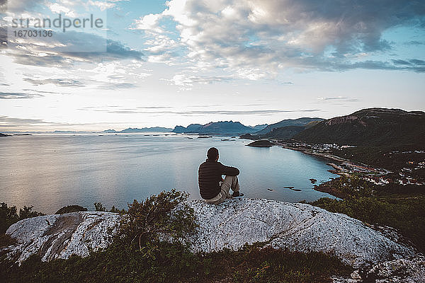 Wanderer sitzt auf einem Felsen und schaut auf Meer und Inseln