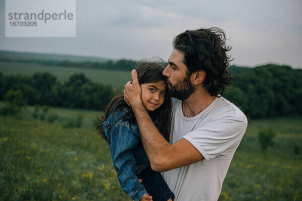 Vater trägt und küsst Tochter im Freien auf einem Feld