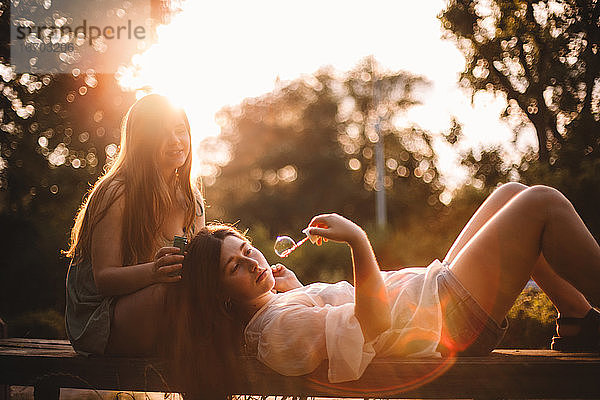 Freundinnen spielen mit Blasen beim Entspannen im Park im Sommer