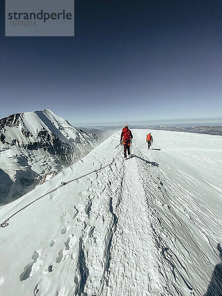 Roped Party beim Abstieg vom Mont Blanc unter dunkelblauem Himmel bei starkem Wind