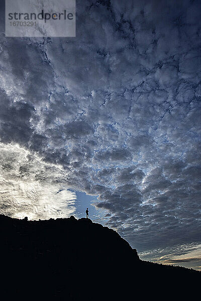 Ein einsamer Wanderer steht auf dem Gipfel in der Silhouette mit dramatischen Wolken.