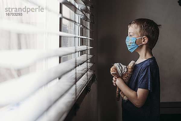 Seitenansicht eines Jungen im Schulalter mit Maske und Stofftier