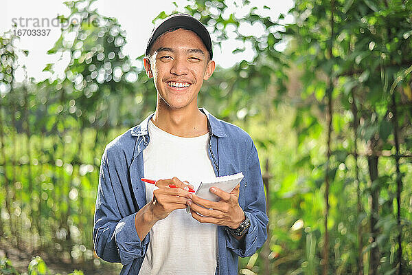 Happy of lächelnd junge asiatische Bauer männlich hält das Notebook auf grünen Garten