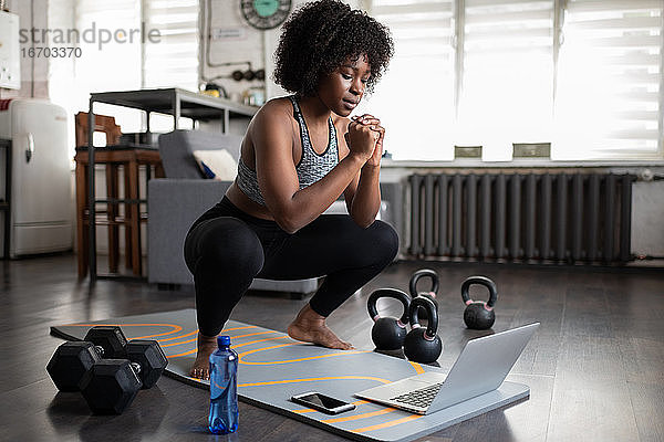 Afroamerikanische Sportlerin in der Hocke beim Online-Workout