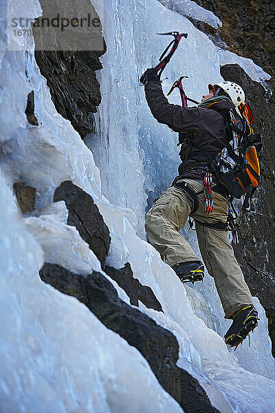 junger Mann klettert auf gefrorenem Wasserfall in Island