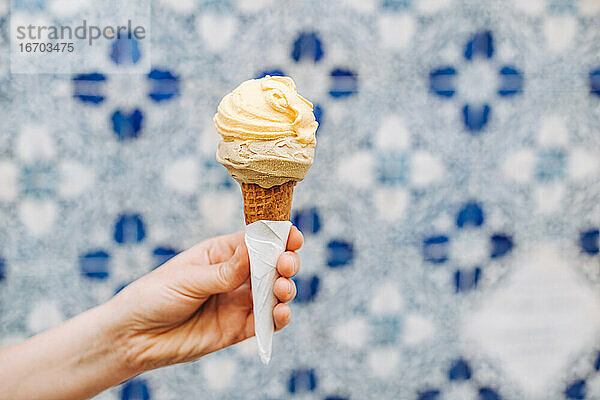 Weibliche Hand hält Eiswaffel auf unscharfem weiß-blauem Hintergrund