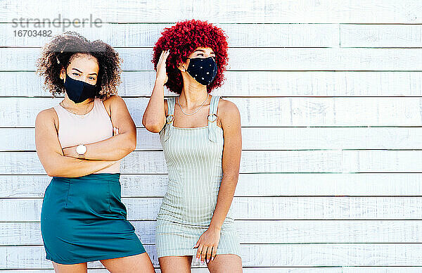 Zwei lateinische Frauen mit Maske in einer sorglosen Haltung auf einem weißen Hintergrund