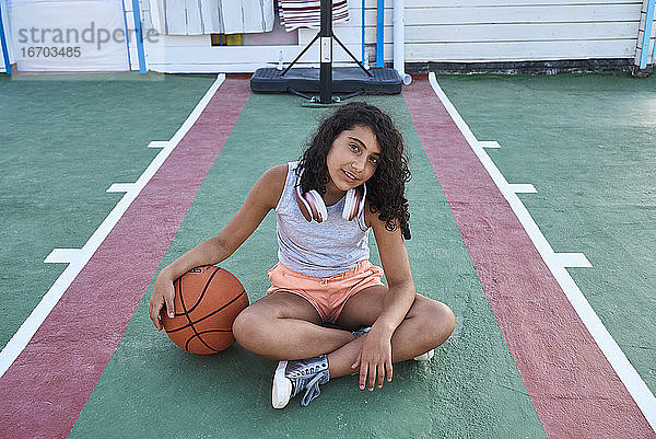 Ein Mädchen sitzt mit einem Basketball vor der Kamera